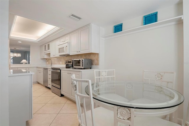 kitchen with light tile patterned floors, a raised ceiling, decorative backsplash, white cabinets, and appliances with stainless steel finishes