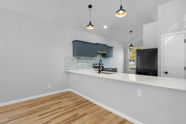 kitchen with black refrigerator, decorative backsplash, vaulted ceiling, blue cabinets, and sink