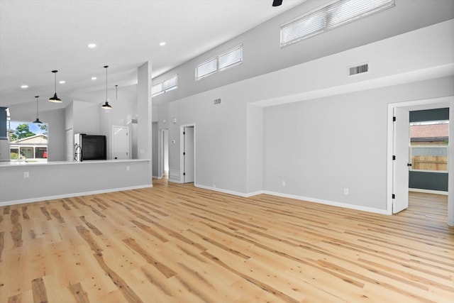 unfurnished living room featuring a towering ceiling and light hardwood / wood-style flooring