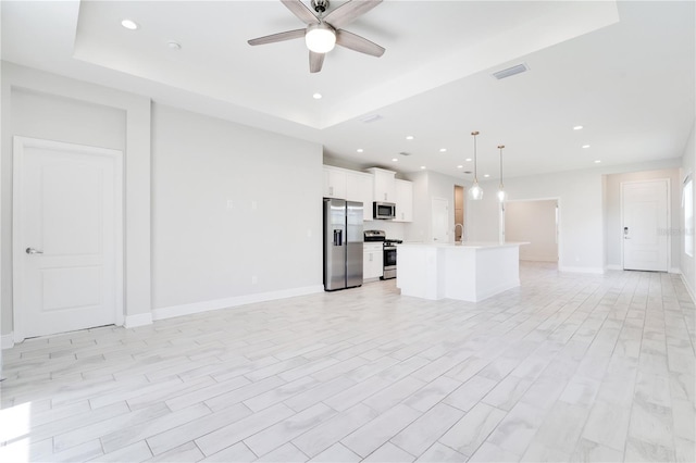 unfurnished living room featuring ceiling fan, light wood-type flooring, and a tray ceiling