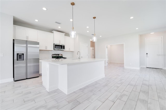 kitchen with white cabinets, appliances with stainless steel finishes, a center island with sink, and pendant lighting