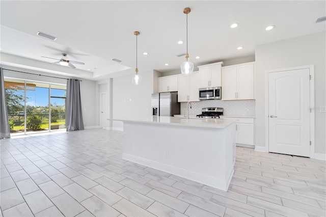 kitchen featuring a center island with sink, ceiling fan, appliances with stainless steel finishes, decorative light fixtures, and white cabinetry