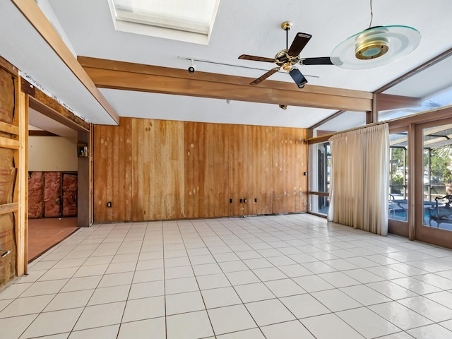 empty room featuring ceiling fan, light tile patterned floors, wooden walls, and beamed ceiling