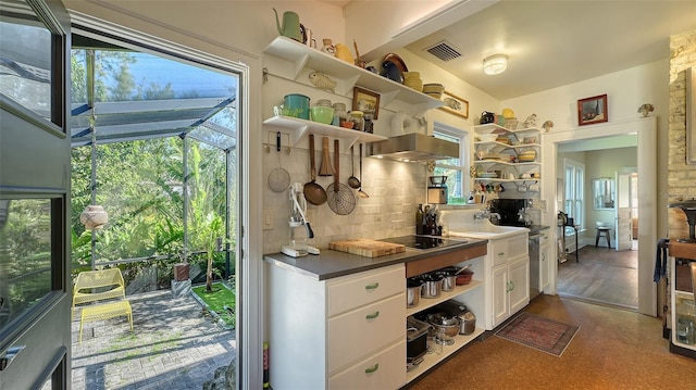 kitchen featuring decorative backsplash, black electric stovetop, white cabinetry, and wall chimney exhaust hood