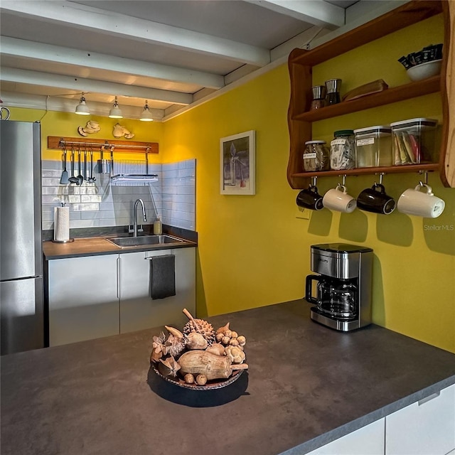 kitchen featuring stainless steel fridge, tasteful backsplash, sink, beam ceiling, and pendant lighting