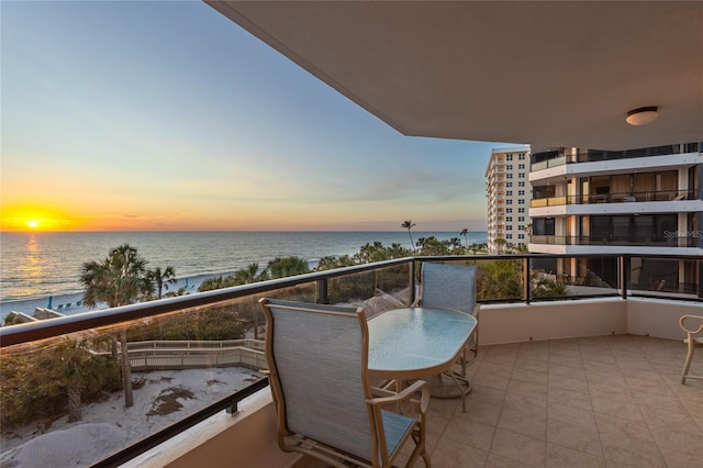 balcony at dusk with a water view and a view of the beach