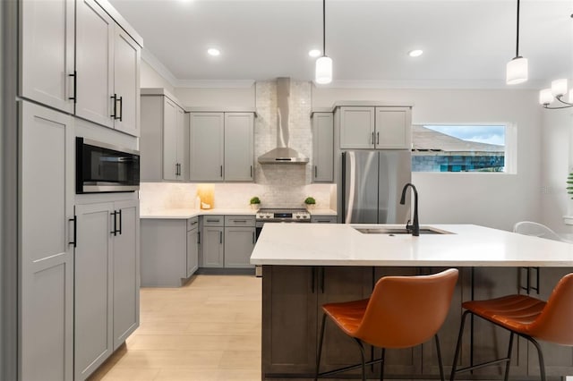 kitchen with a sink, appliances with stainless steel finishes, gray cabinets, decorative backsplash, and wall chimney exhaust hood