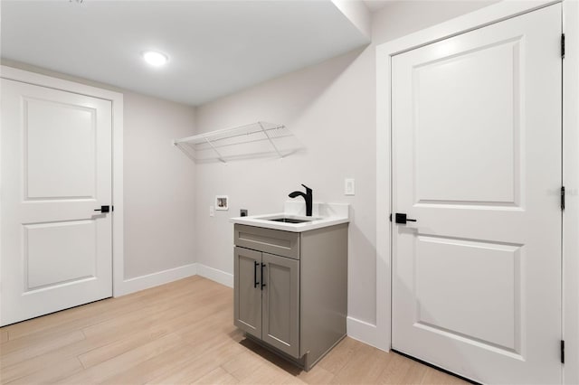 washroom with washer hookup, a sink, light wood-style flooring, and baseboards