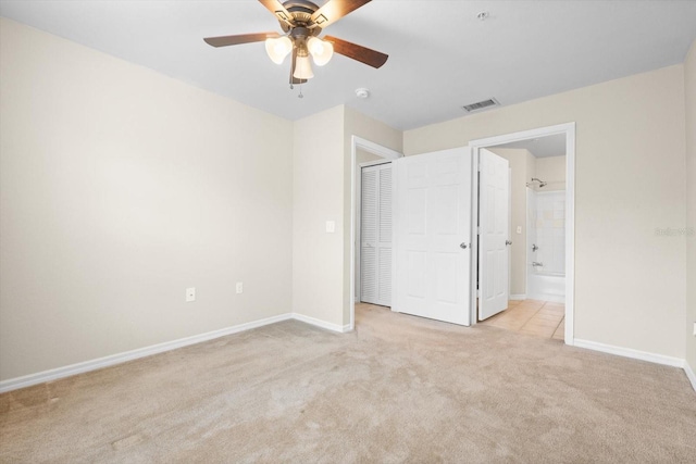 unfurnished bedroom featuring light carpet, a closet, ensuite bath, and ceiling fan