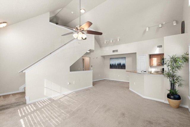 unfurnished living room featuring rail lighting, ceiling fan, light carpet, and high vaulted ceiling