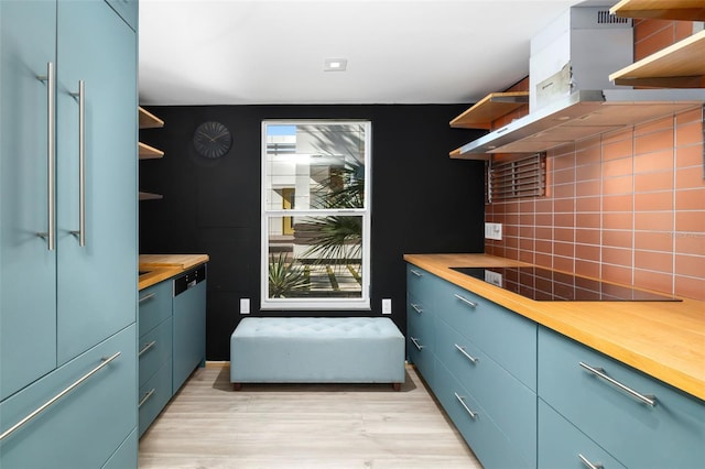 kitchen featuring black electric stovetop, wall chimney exhaust hood, tasteful backsplash, and wooden counters