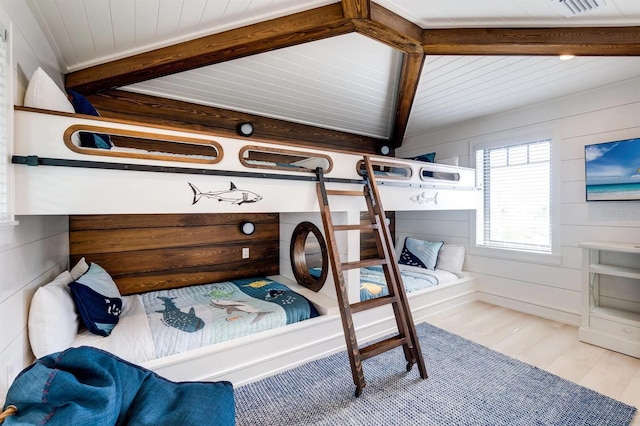 bedroom with light hardwood / wood-style flooring, lofted ceiling with beams, and wooden walls