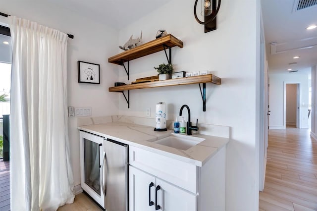 bar with stainless steel refrigerator, white cabinetry, sink, light stone countertops, and light wood-type flooring