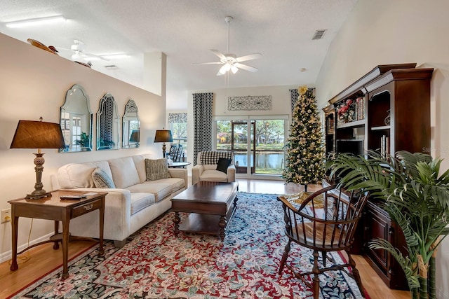 living room featuring ceiling fan, lofted ceiling, a textured ceiling, and light hardwood / wood-style flooring