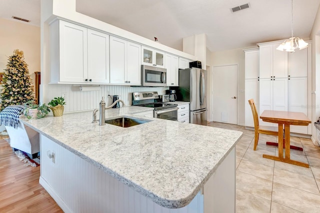 kitchen featuring kitchen peninsula, appliances with stainless steel finishes, sink, decorative light fixtures, and white cabinetry