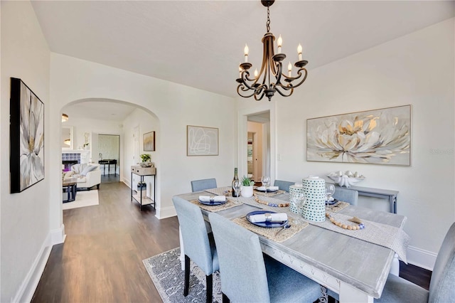 dining space featuring a fireplace, dark wood-type flooring, and an inviting chandelier