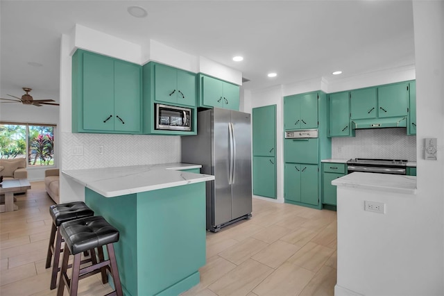 kitchen with kitchen peninsula, a kitchen breakfast bar, stainless steel appliances, ceiling fan, and green cabinetry