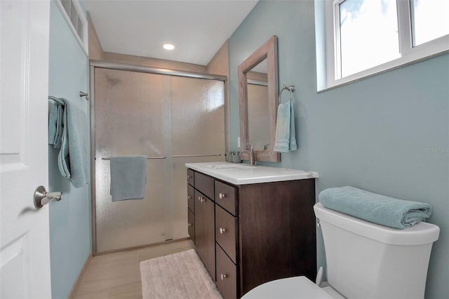 bathroom featuring a shower with door, vanity, and toilet