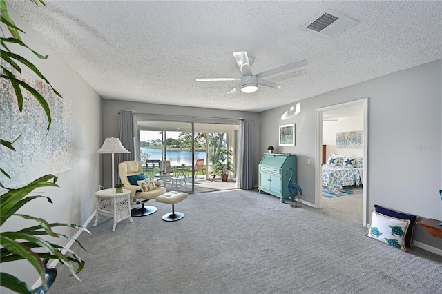 living area with light carpet, a water view, visible vents, baseboards, and a ceiling fan