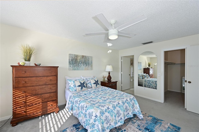 bedroom with light carpet, visible vents, arched walkways, a spacious closet, and a textured ceiling