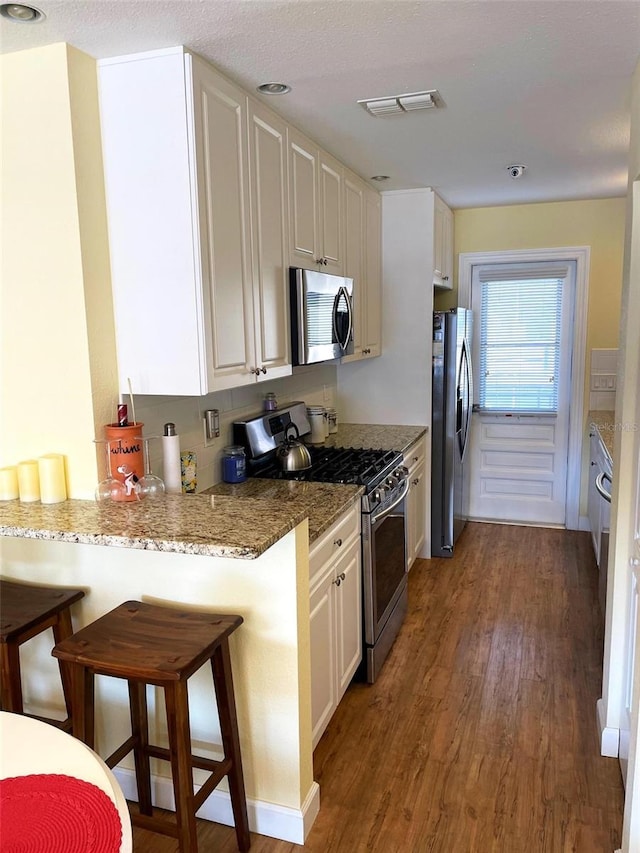 kitchen featuring stainless steel appliances, kitchen peninsula, stone countertops, a kitchen bar, and white cabinets