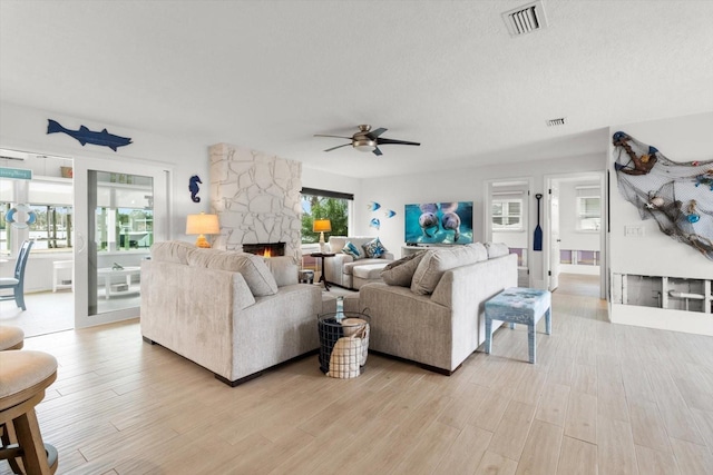 living room featuring a fireplace, a textured ceiling, light hardwood / wood-style flooring, and ceiling fan