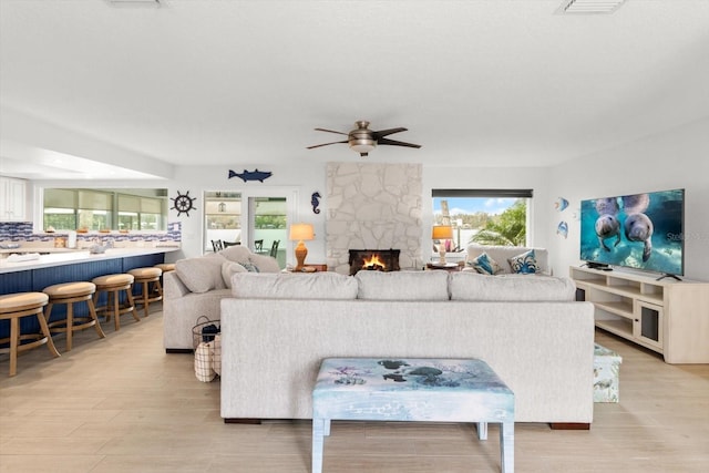 living room featuring ceiling fan, a fireplace, a healthy amount of sunlight, and light hardwood / wood-style floors