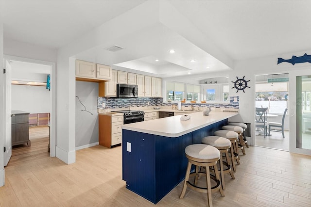 kitchen with a breakfast bar, light hardwood / wood-style flooring, appliances with stainless steel finishes, tasteful backsplash, and kitchen peninsula