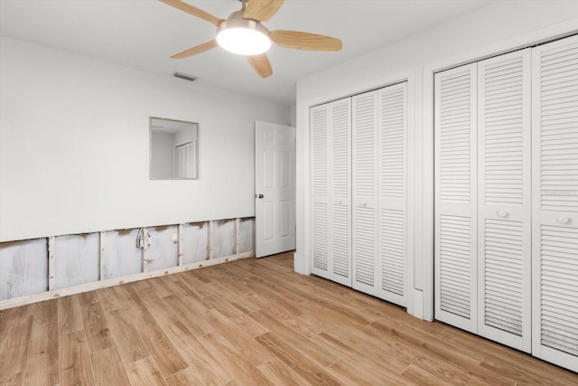 unfurnished bedroom featuring ceiling fan, two closets, and light wood-type flooring