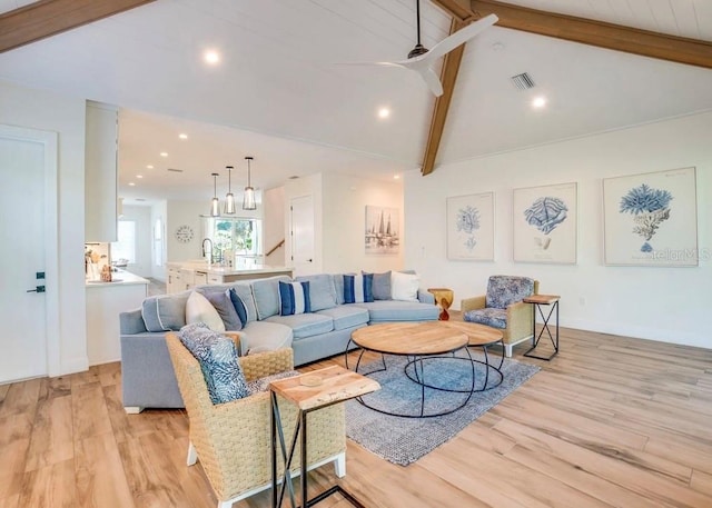 living room featuring ceiling fan, light hardwood / wood-style floors, and vaulted ceiling with beams