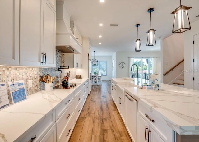 kitchen with white cabinetry, light stone countertops, custom exhaust hood, and pendant lighting