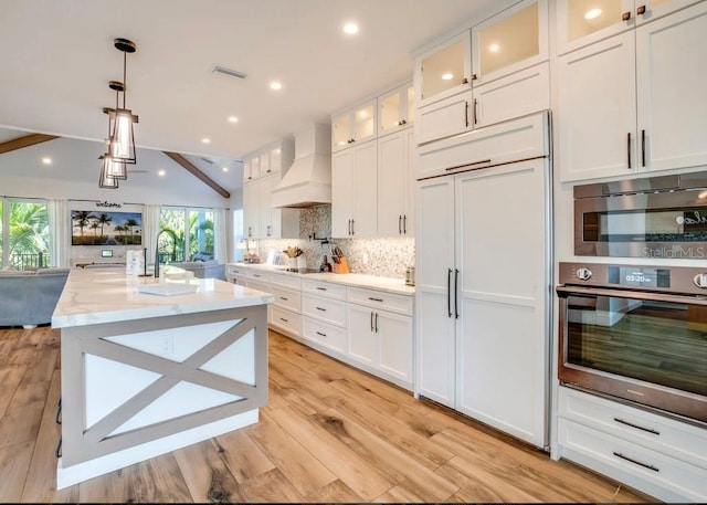 kitchen featuring custom exhaust hood, white cabinetry, light stone counters, hanging light fixtures, and stainless steel appliances