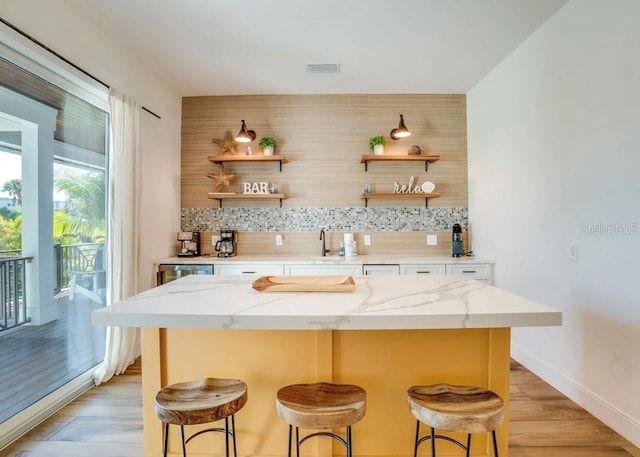 bar featuring light stone counters, sink, decorative backsplash, and light hardwood / wood-style flooring