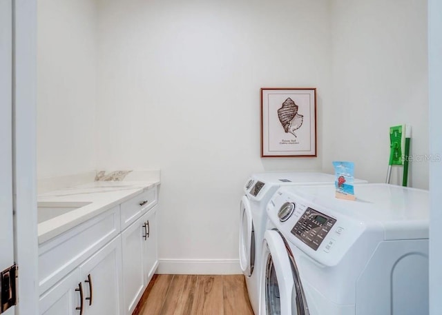 clothes washing area with light hardwood / wood-style floors, washing machine and dryer, and cabinets