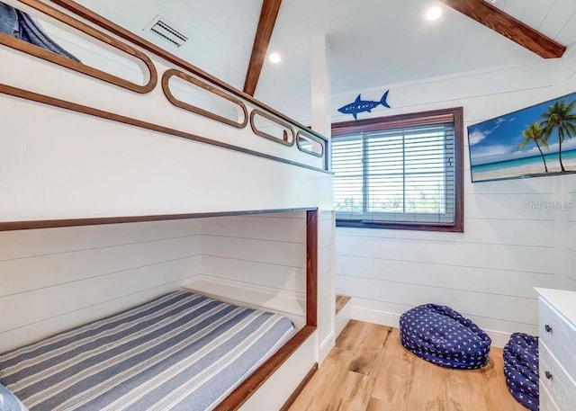 bedroom with beamed ceiling, light hardwood / wood-style floors, and wood walls