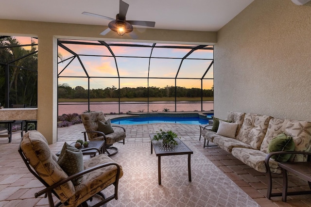 patio terrace at dusk with an outdoor hangout area, a water view, ceiling fan, and a lanai