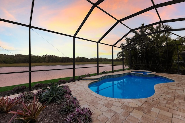 pool at dusk featuring an in ground hot tub, a patio, a water view, and glass enclosure