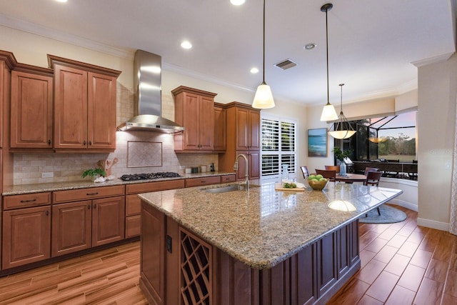 kitchen featuring sink, wall chimney exhaust hood, a kitchen breakfast bar, stainless steel gas stovetop, and a kitchen island with sink