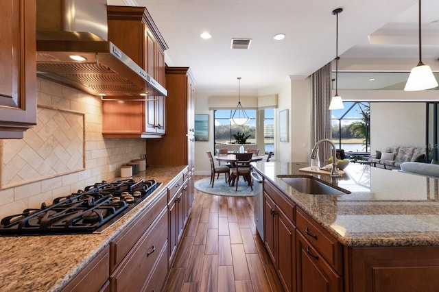 kitchen with black gas cooktop, sink, wall chimney exhaust hood, and hanging light fixtures