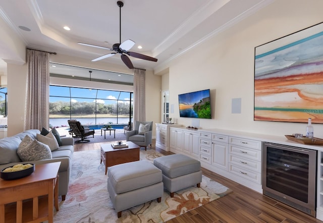 living room featuring hardwood / wood-style floors, a raised ceiling, beverage cooler, and ornamental molding