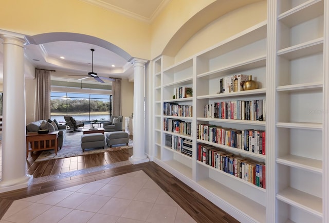 sitting room with light wood-type flooring, decorative columns, built in shelves, a tray ceiling, and ceiling fan