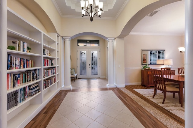 foyer featuring french doors, light hardwood / wood-style flooring, a notable chandelier, decorative columns, and crown molding