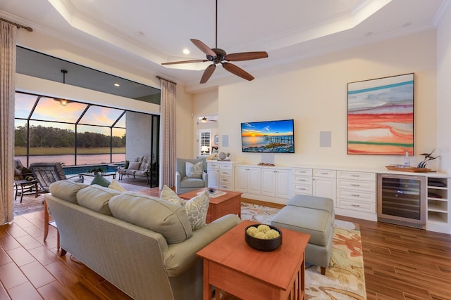 living room with wine cooler, a tray ceiling, ornamental molding, and ceiling fan