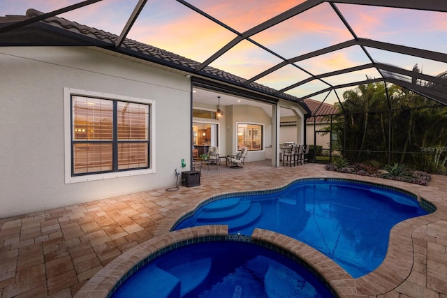 pool at dusk with an in ground hot tub, a lanai, ceiling fan, and a patio area