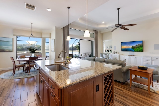 kitchen with dark hardwood / wood-style floors, decorative light fixtures, an island with sink, sink, and light stone counters