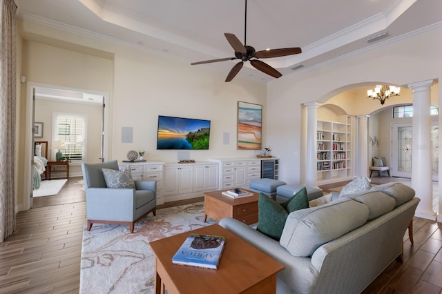 living room featuring decorative columns, a tray ceiling, ornamental molding, light hardwood / wood-style floors, and beverage cooler