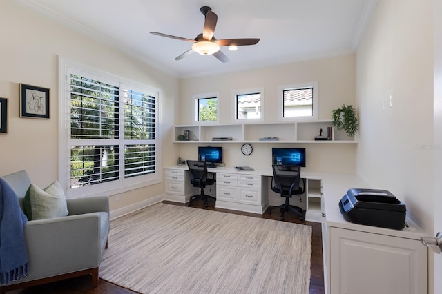 office area with built in desk, crown molding, baseboards, dark wood finished floors, and ceiling fan