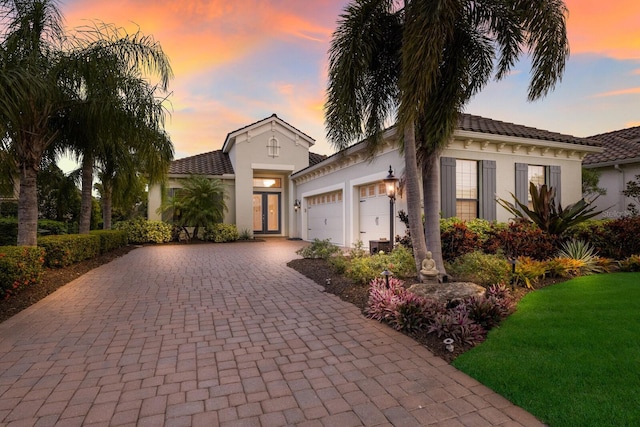 mediterranean / spanish house with decorative driveway, a tiled roof, stucco siding, and an attached garage