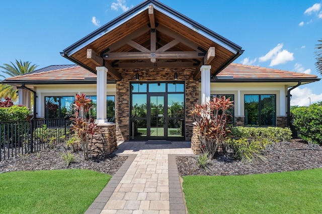 doorway to property with stucco siding, fence, french doors, stone siding, and a tiled roof