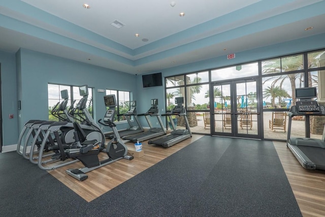 exercise room with visible vents, baseboards, wood finished floors, a raised ceiling, and french doors